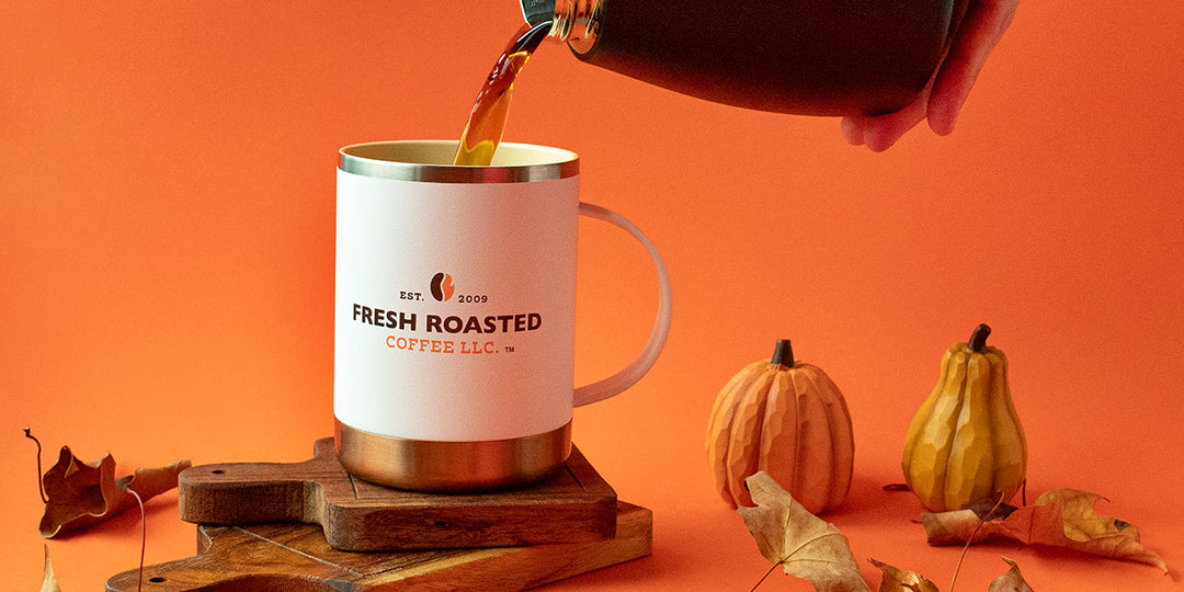 An Asobu Ultimate Mug on a stack of serving blocks with coffee pouring in, surrounded by autumn leaves.