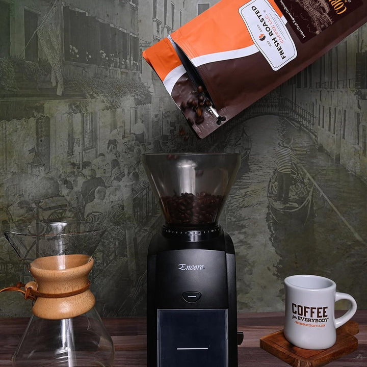 Fresh Roasted Coffee Correggio whole beans being poured into a coffee grinder, ready for a fresh Italian espresso brew.