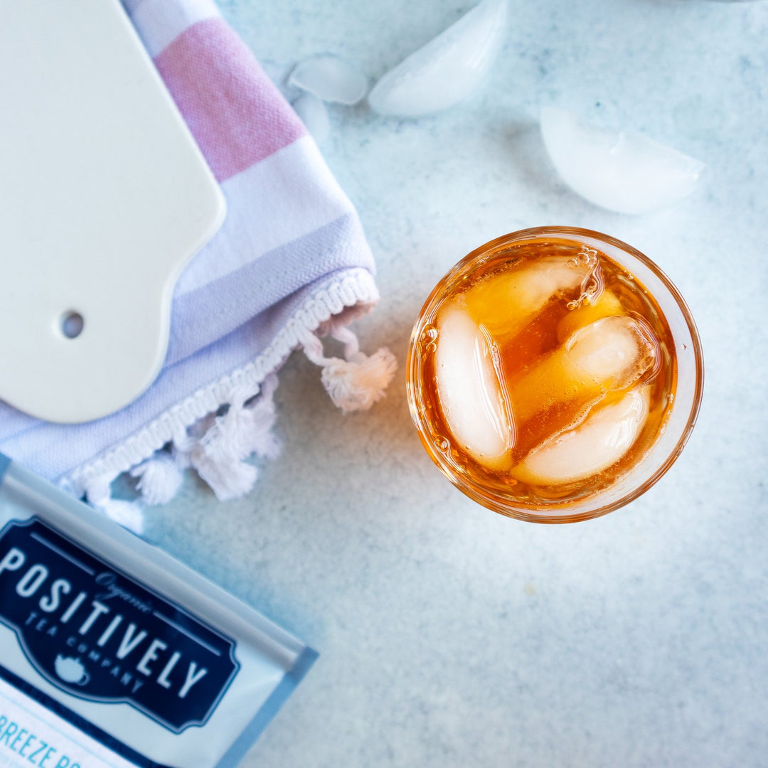 Positively Tea Company Island Breeze Rooibos tea served iced in a clear glass, showcasing its bright tropical color and refreshing flavor.