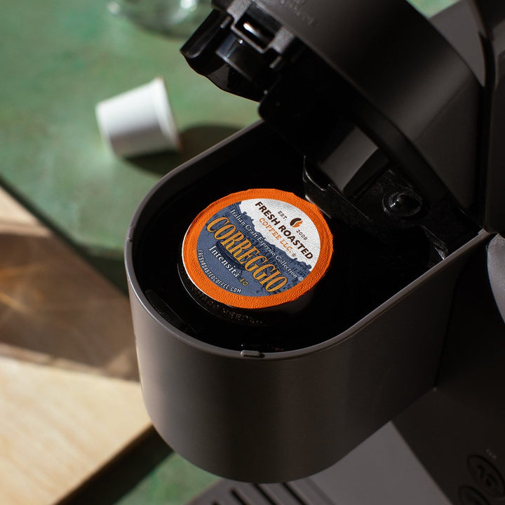 Fresh Roasted Coffee Correggio espresso pod placed inside a single-serve coffee machine, ready for brewing a bold Italian roast cup.